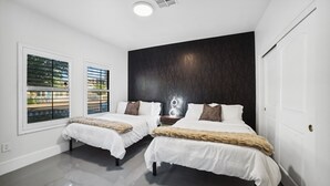 Un dormitorio moderno con dos camas, una pared de acento oscura y ventanas amplias con persianas.
