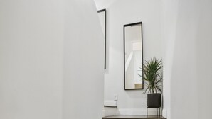 Una escalera de madera con paredes blancas que lleva a una plataforma con una planta en maceta y un espejo.
