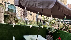 An outdoor patio with a table and chairs, a green hedge, and a potted plant.