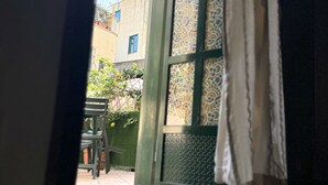 A room with a glass table, a view of the outside through a window with patterned curtains, and a glimpse of outdoor furniture.