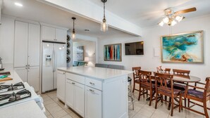 A modern kitchen with white cabinetry, a central island, and a dining area with wooden chairs and a table. - The MCM House walk2 FIFA Dallas Stadium~ AT&T!  Best Arlington vacation rentals! (Arlington)