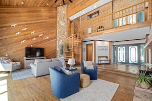 A spacious living area with a wooden ceiling, a stone accent wall, a staircase, and a television.