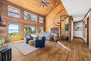 A spacious living area with a wooden interior, a spiral staircase, and large windows offering a view of the outdoors.