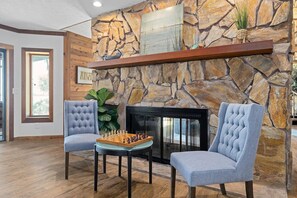 A room with a stone wall, a fireplace, two upholstered chairs, and a chessboard.