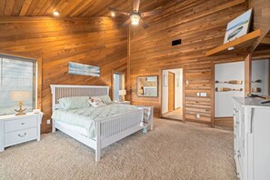 A bedroom with a wooden ceiling, a bed, a nightstand, a dresser, and a window with blinds.