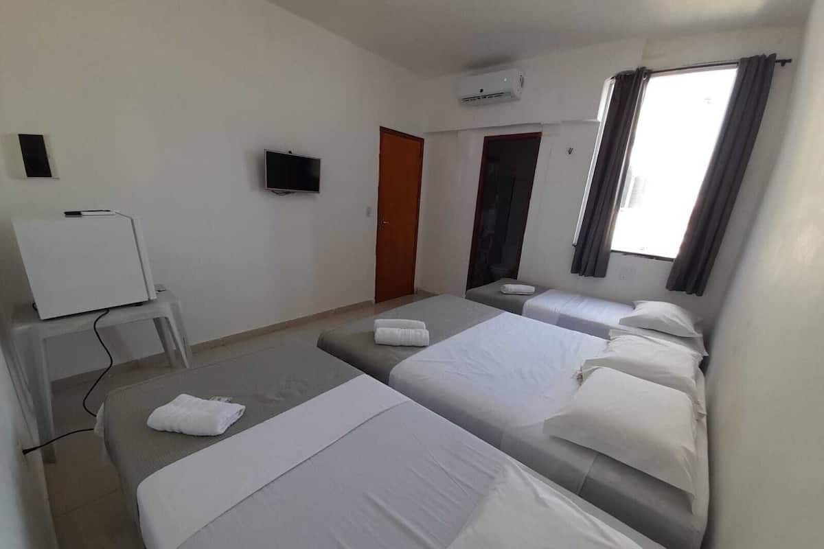 A hotel room with two beds, a TV, a desk, and an air conditioner.