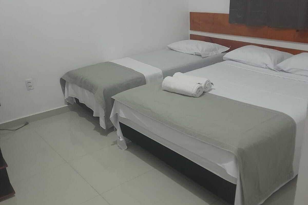 A hotel room with two single beds, a wooden headboard, and a tiled floor.