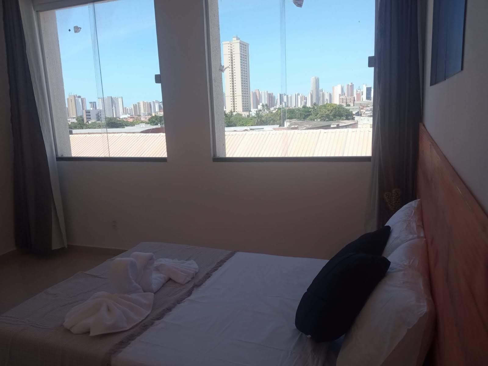 A hotel room with a bed, a window, and a view of a cityscape.