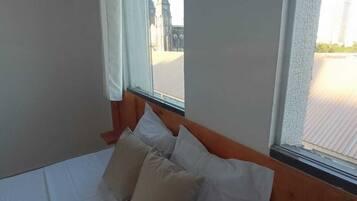 Una cama con ropa de cama blanca y almohadas color beige en una habitación con ventana.