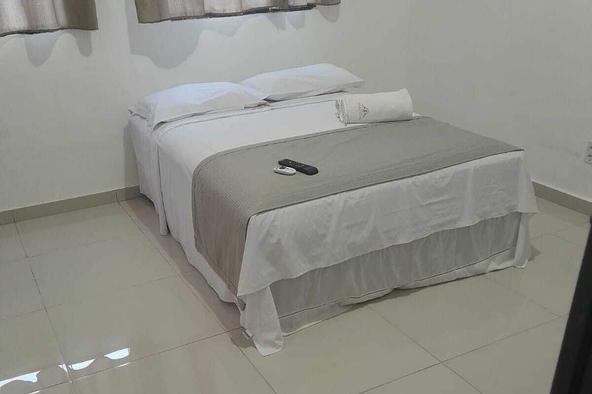 A bedroom with a bed, a remote control, and a window with curtains.