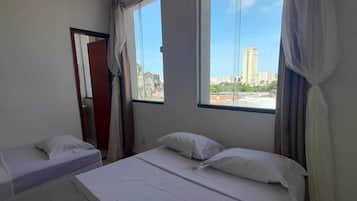 A hotel room with two single beds, a large window with a city view, and a door leading to another room.