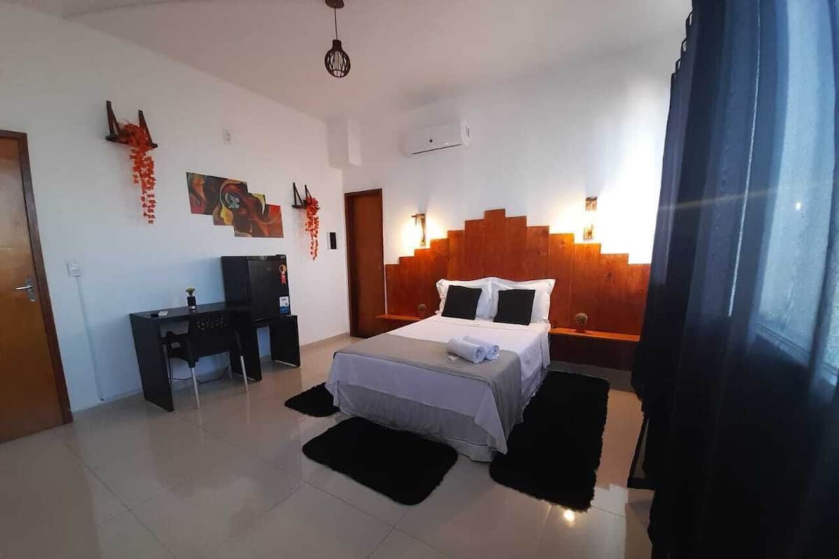 A bedroom with a bed, a desk, and a chair. There are wall decorations and a window with curtains.