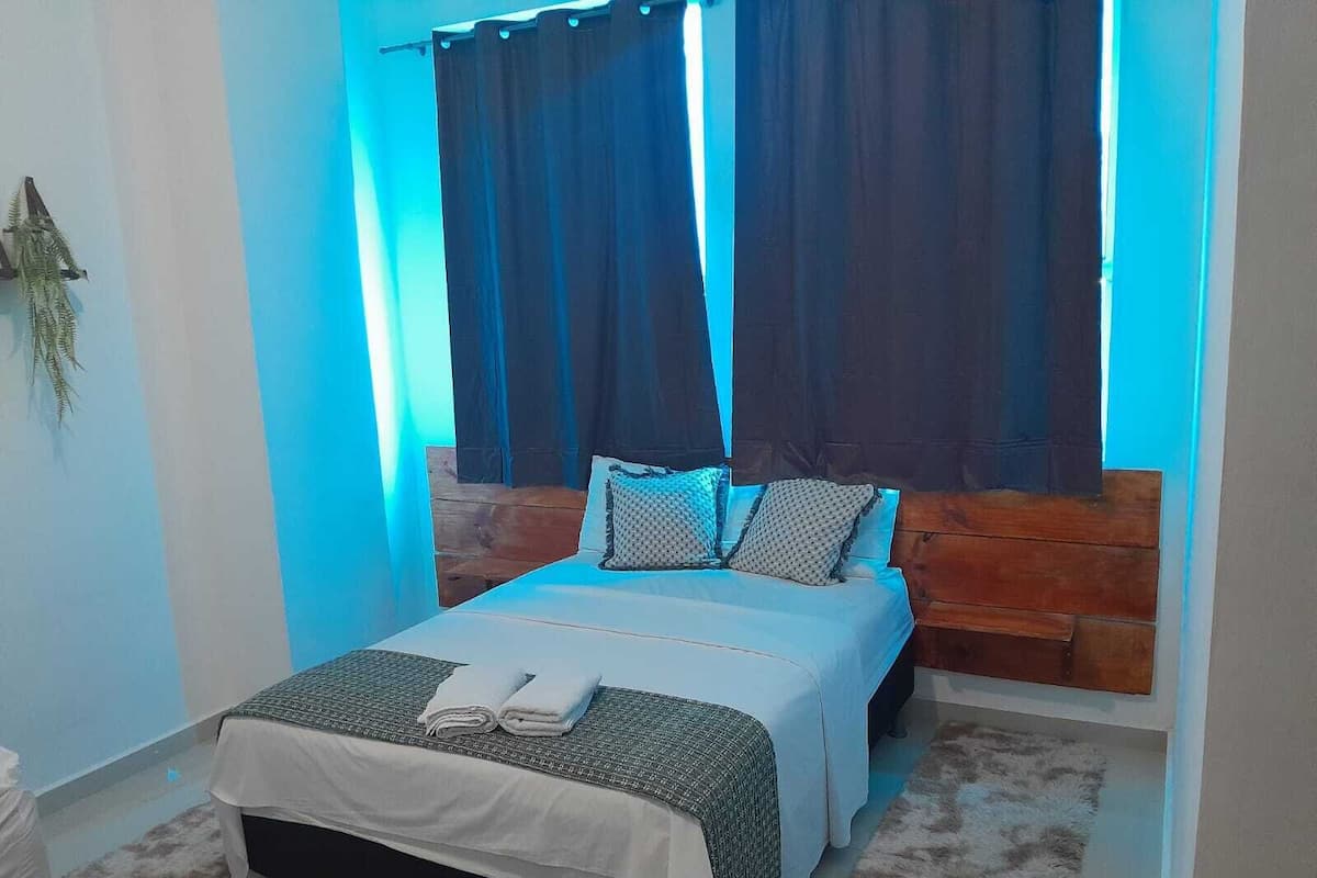 A bedroom with a wooden headboard, a bed with white bedding, two pillows, and a blanket.