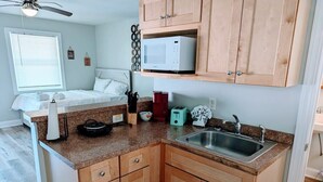 A compact kitchen with wooden cabinets, a microwave, a sink, and a countertop with various kitchen items. - Relaxing Studio Apt - Central MB (Myrtle Beach)