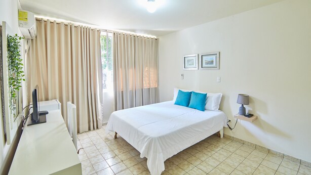 A hotel room with a bed, a desk with a computer, a lamp, and a window with curtains.
