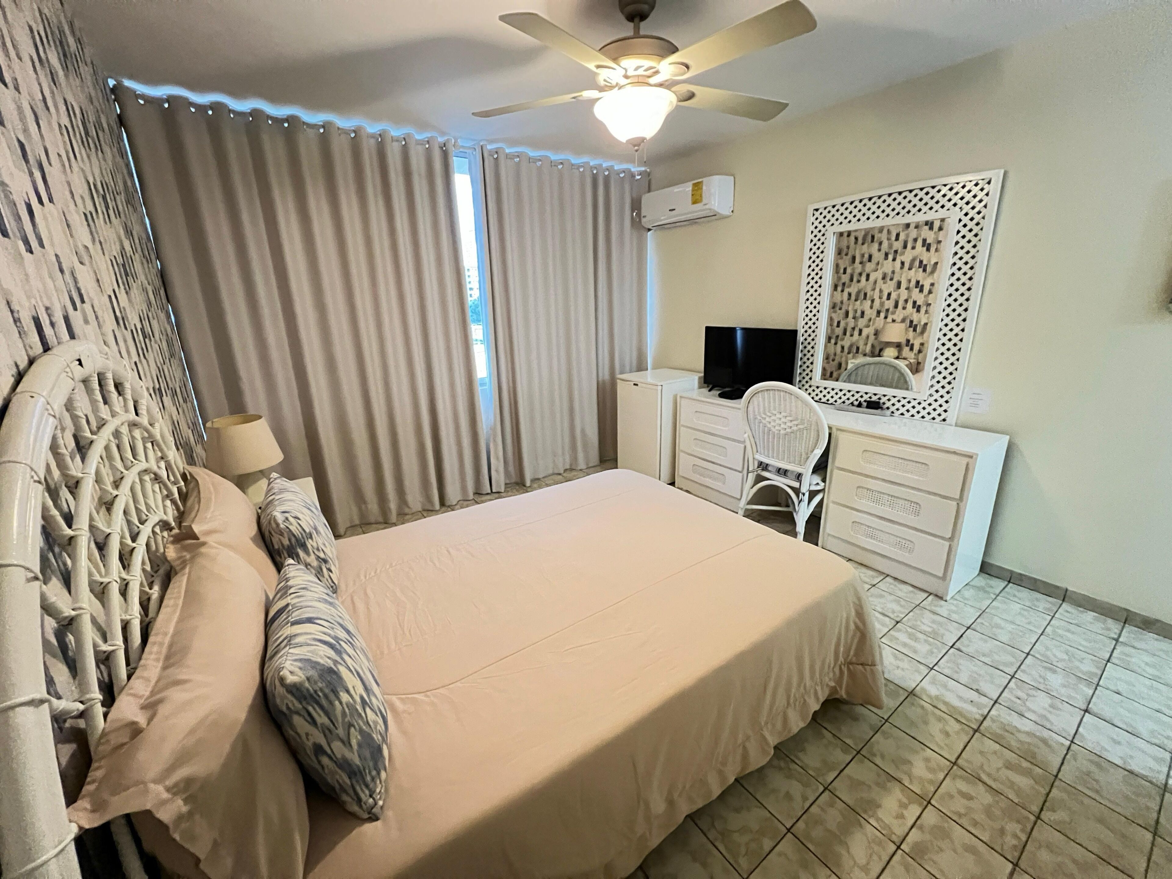 A bedroom with a bed, a desk with a chair, a ceiling fan, and an air conditioning unit.