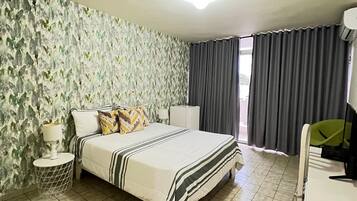 Quarto com uma cama, mesa de cabeceira, luminária, cômoda e uma janela com cortinas.