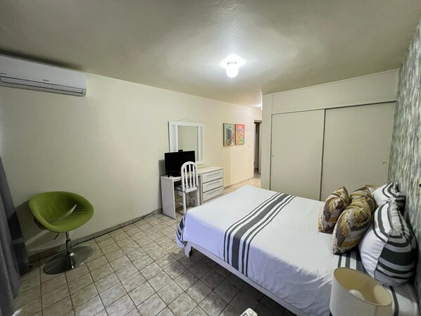 A bedroom with a bed, a chair, a dresser, a mirror, and a wardrobe.