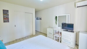 A hotel room with a bed, a dresser, a television, and an air conditioning unit.