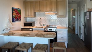 A modern kitchen with light wood cabinets, a white island with stools, a microwave, and a stainless steel stove. - 3rd Floor Oceanfront Condo!! Community Pool & 1000 ft Fishing Pier! *Unit 308, Bldg A* (Isle Of Palms)