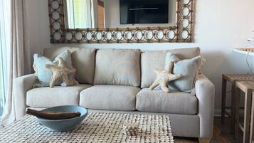A living room with a sofa, a coffee table, a decorative mirror, and a television.