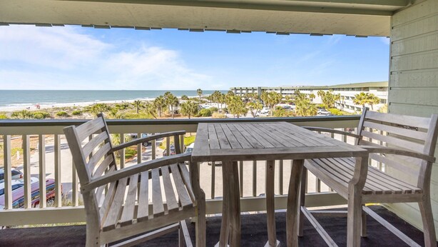 A wooden balcony with a table and chairs overlooking a beach and a parking area. - 3rd Floor Oceanfront Condo!! Community Pool & 1000 ft Fishing Pier! *Unit 308, Bldg A* (Isle Of Palms)