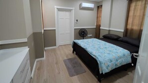 A bedroom with a bed, a fan, an air conditioning unit, a door, and a small rug.