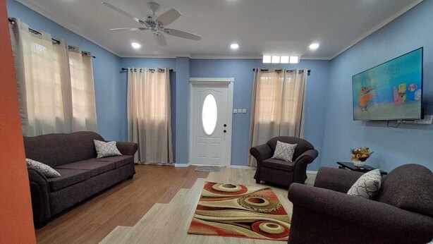 A living room with two sofas, a chair, a ceiling fan, and a television on the wall.