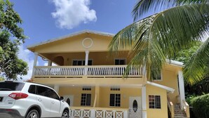 A two-story building with a balcony, a car parked in front, and a palm tree.