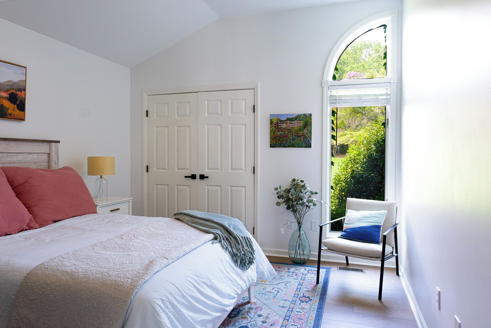 Une chambre à coucher avec un lit, une chaise, une porte et une fenêtre donnant sur un paysage verdoyant.
