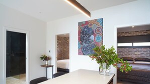 A modern room with a bed, a dining table, and a large abstract painting on the wall. - Cockatoo Cottage Bundeena (Bundeena)