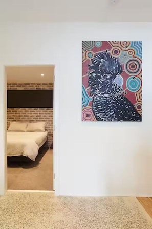 A room with a bed, a wall with a colorful abstract painting, and a door leading to another room.