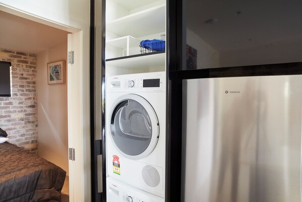 Een kleine kamer met een wasmachine, een bed en een bakstenen muur.