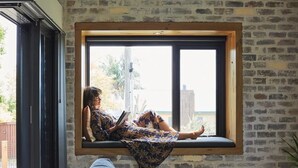 A person sitting on a window seat reading a book, with a brick wall and a window in the background. - Cockatoo Cottage Bundeena (Bundeena)