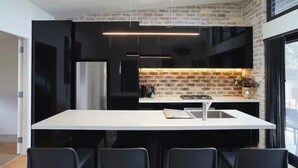 A modern kitchen with a central island, black cabinetry, and a brick accent wall. - Cockatoo Cottage Bundeena (Bundeena)