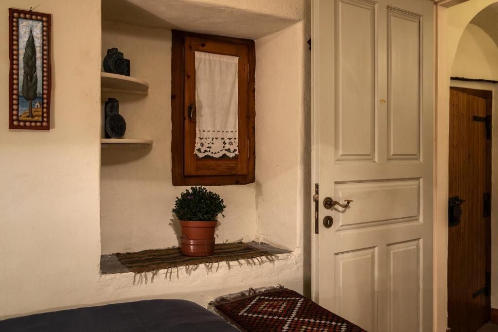 Een kamer met een houten deur, een klein plankje met decoratieve objecten, een potplant en een lijst met een foto aan de muur.