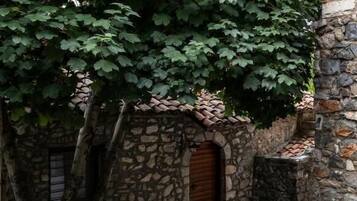 Un edificio de piedra con techo de tejas, un jarrón grande y un árbol de hojas verdes.