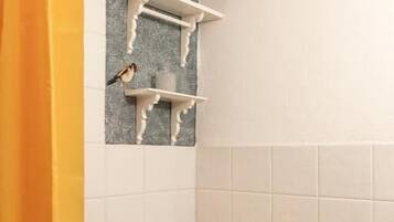 Une salle de bain avec des toilettes, des murs recouverts de carreaux blancs et une étagère sur laquelle se trouvent un pot de fleurs et une statuette d'oiseau.