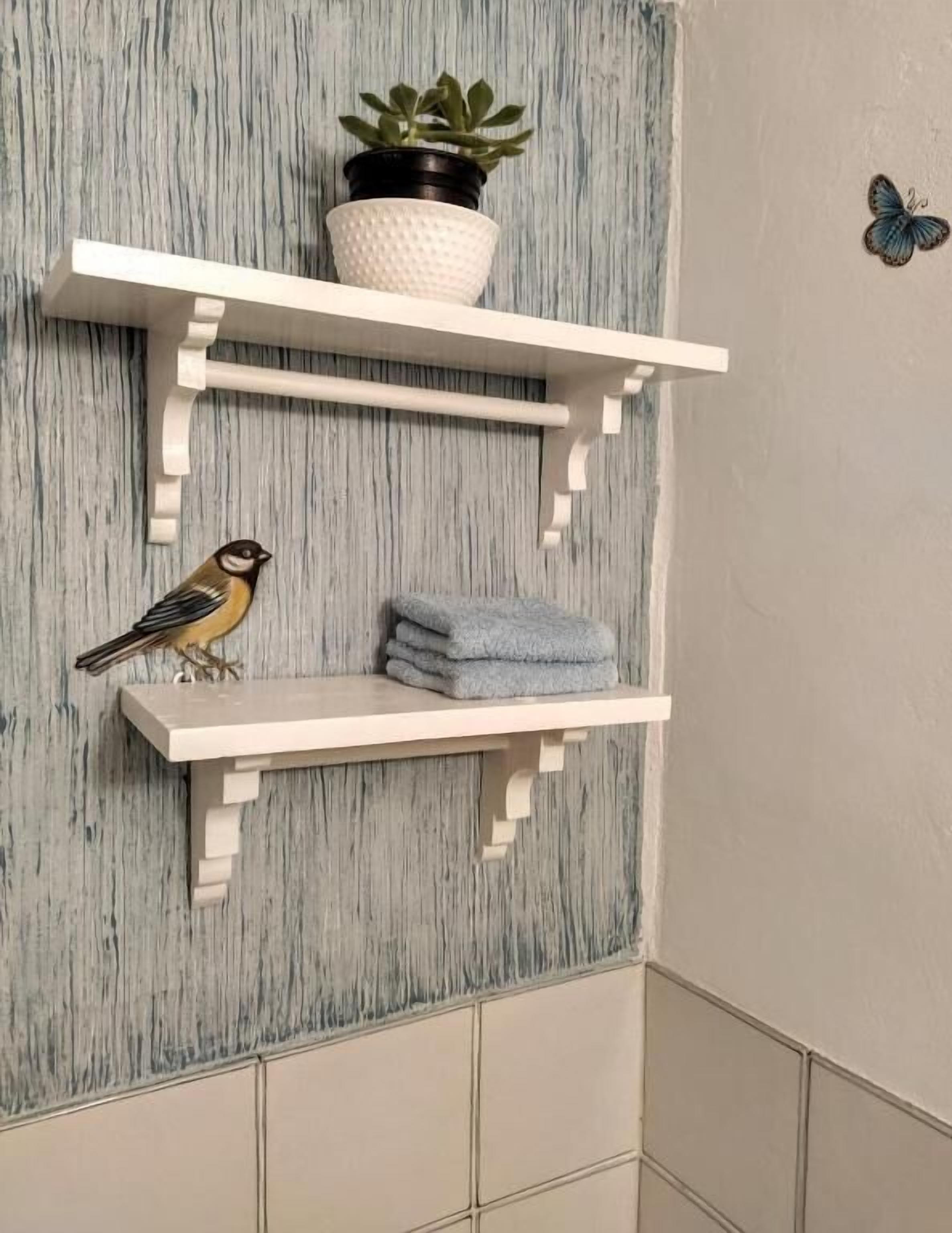 Une salle de bain avec un mur texturé, une étagère blanche ornée d’une plante en pot, des serviettes pliées et un autocollant décoratif en forme de papillon.