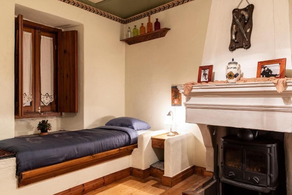 Ein gemütliches Zimmer mit einem Bett, einem kleinen Tisch mit Lampe, einem Regal mit Flaschen, einem Kamin und einem Spiegel.