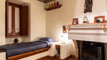 Ein gemütliches Zimmer mit einem Bett, einem kleinen Tisch mit Lampe, einem Regal mit Flaschen, einem Kamin und einem Spiegel.