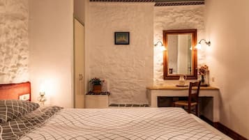 A bedroom with a bed, a desk with a mirror, and a small potted plant.