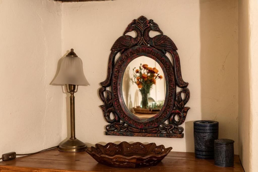 A wooden table with a lamp, a decorative mirror, and two cylindrical containers.