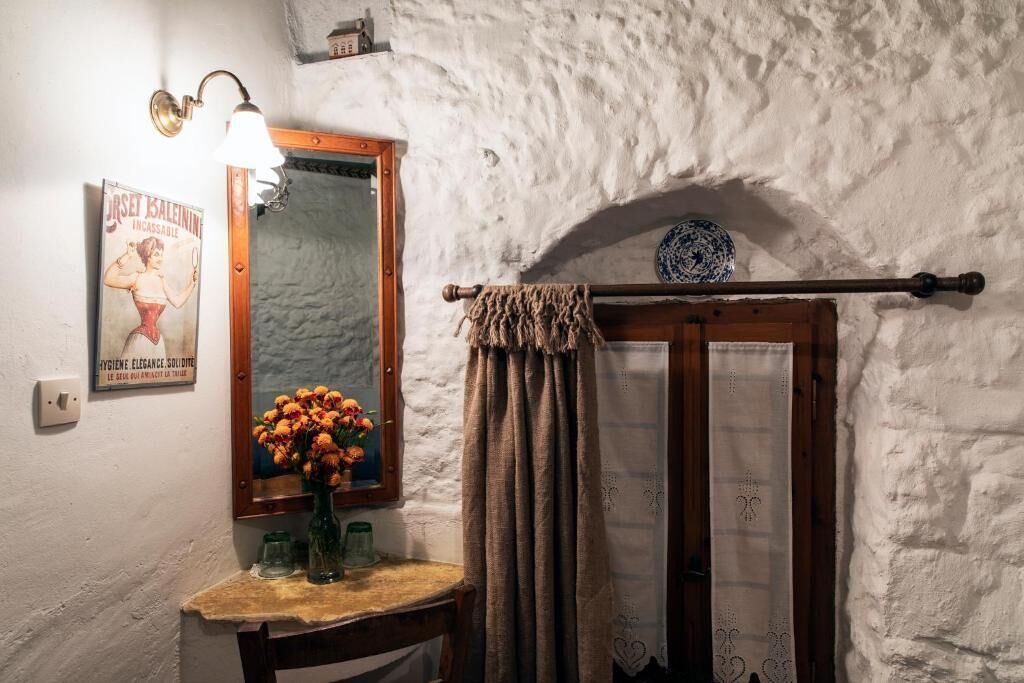 Un baño rústico con pared de piedra, espejo con marco de madera, toallero y un cartel antiguo.