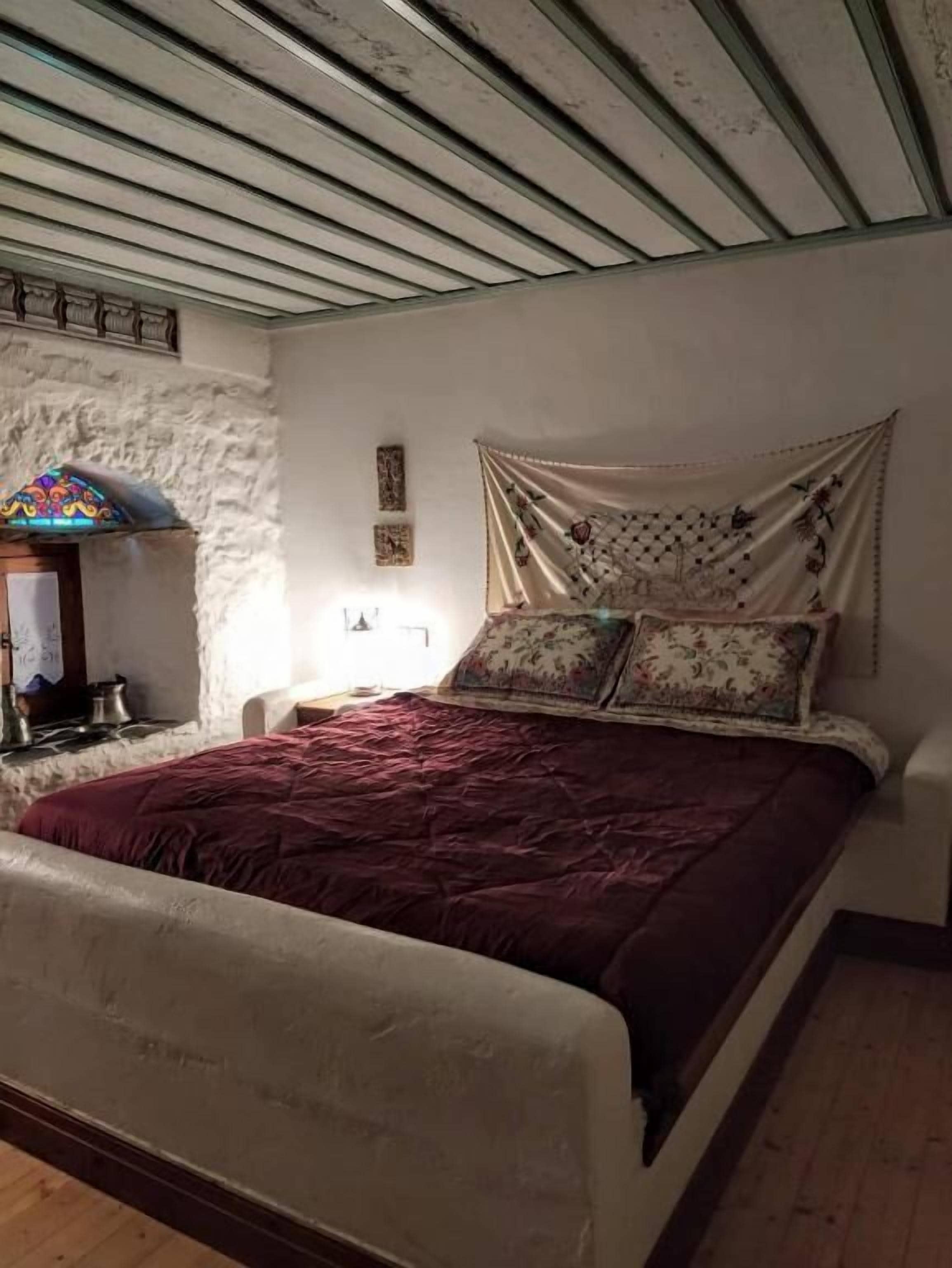 Un dormitorio con cama, mesita de noche, lámpara y estante de pared.