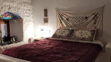 Un dormitorio con cama, mesita de noche, lámpara y estante de pared.