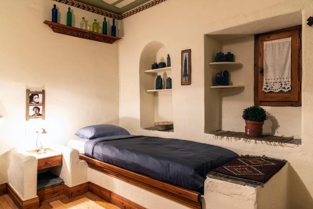 A small, cozy bedroom with a single bed, a nightstand, a dresser, and shelves with decorative items.