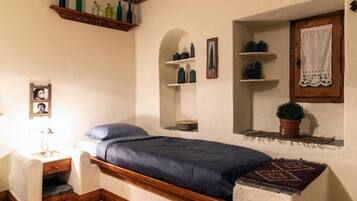A small, cozy bedroom with a single bed, a nightstand, a dresser, and shelves with decorative items.