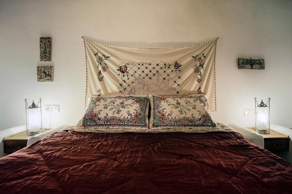 Una cama con cabecera estampada, dos mesitas de noche con lámparas y cuadros en la pared.