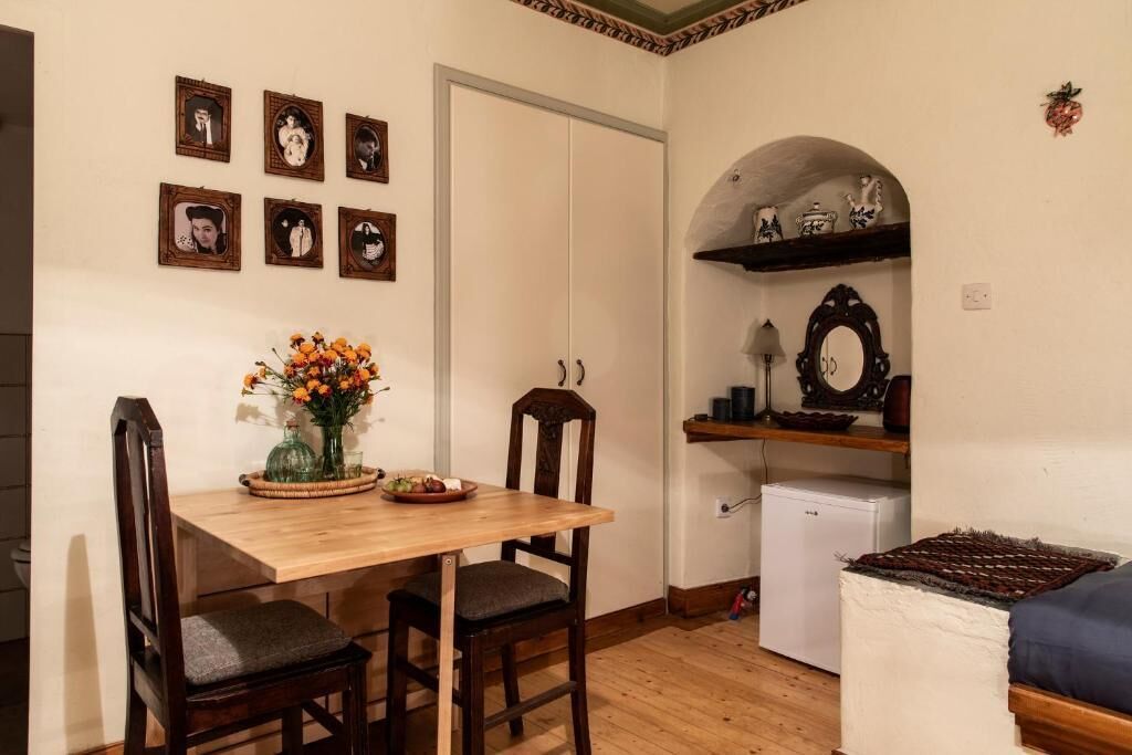 Un comedor con mesa y sillas de madera, un jarrón con flores y un refrigerador.